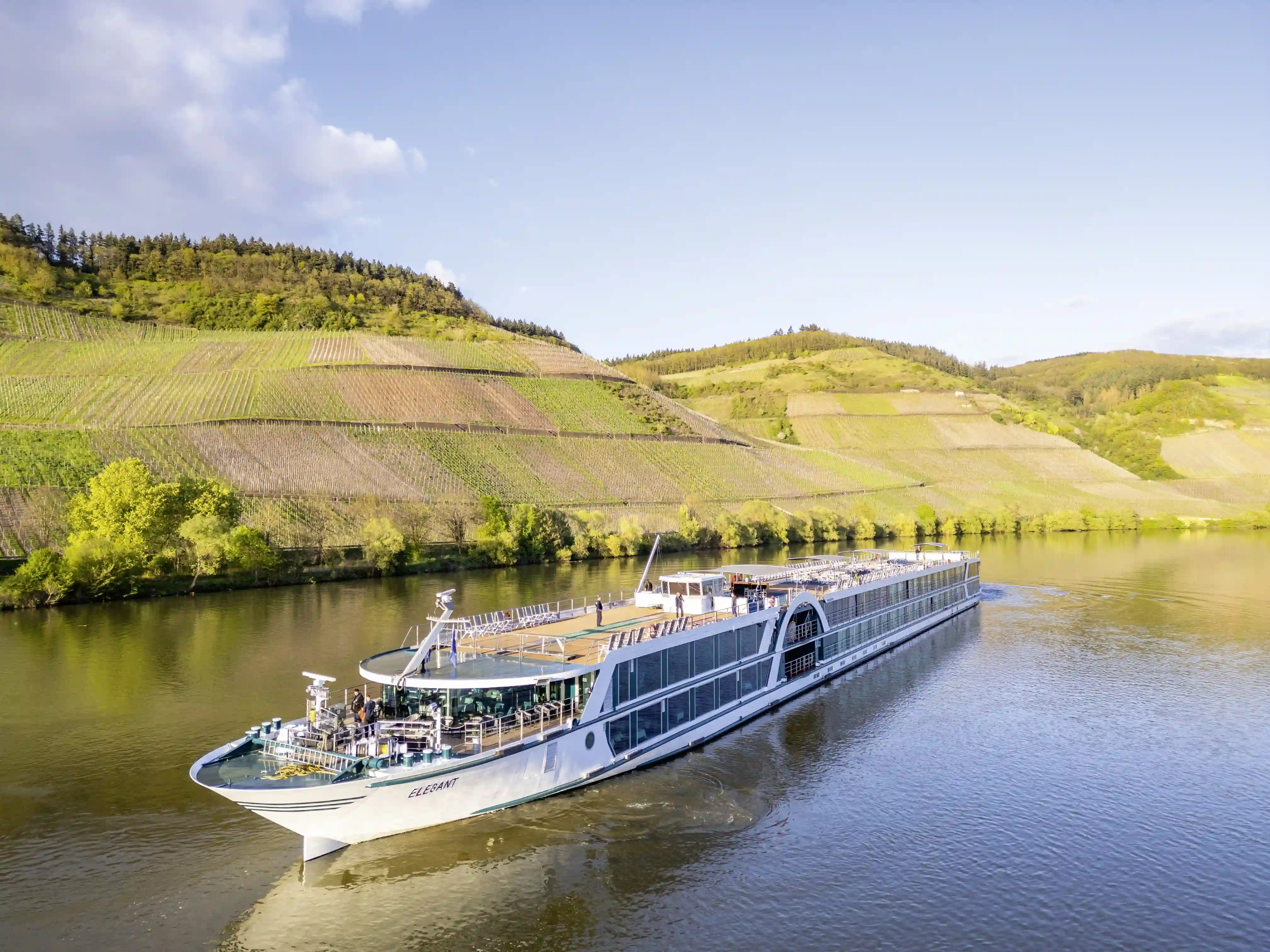 Flusskreuzfahrtschiff Elegant fährt auf einem ruhigen Fluss entlang terrassierter Weinberge bei sonnigem Wetter