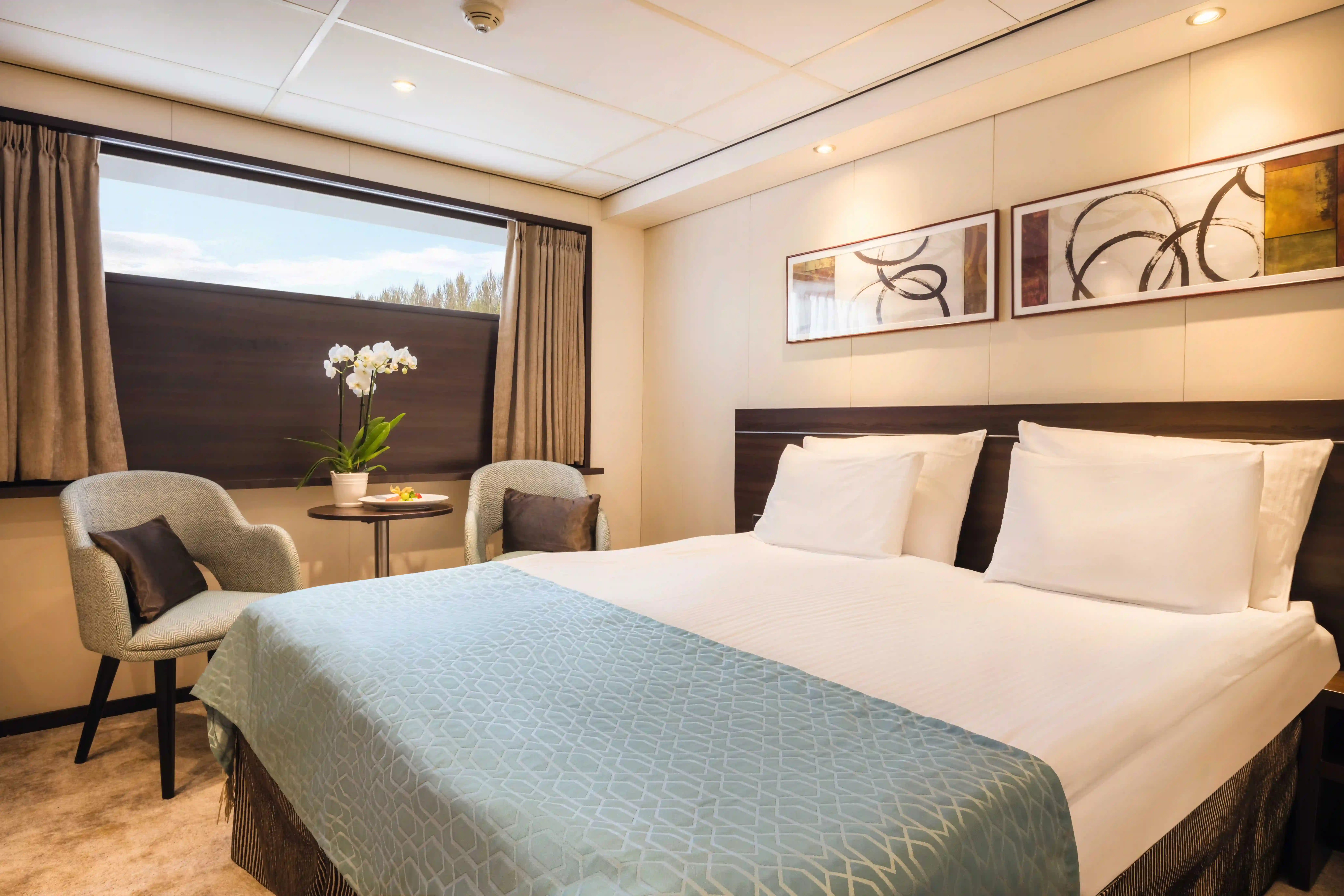 Kabine mit Doppelbett, Fenster, Sesseln, kleiner Sitzgruppe und geschmackvoller Beleuchtung