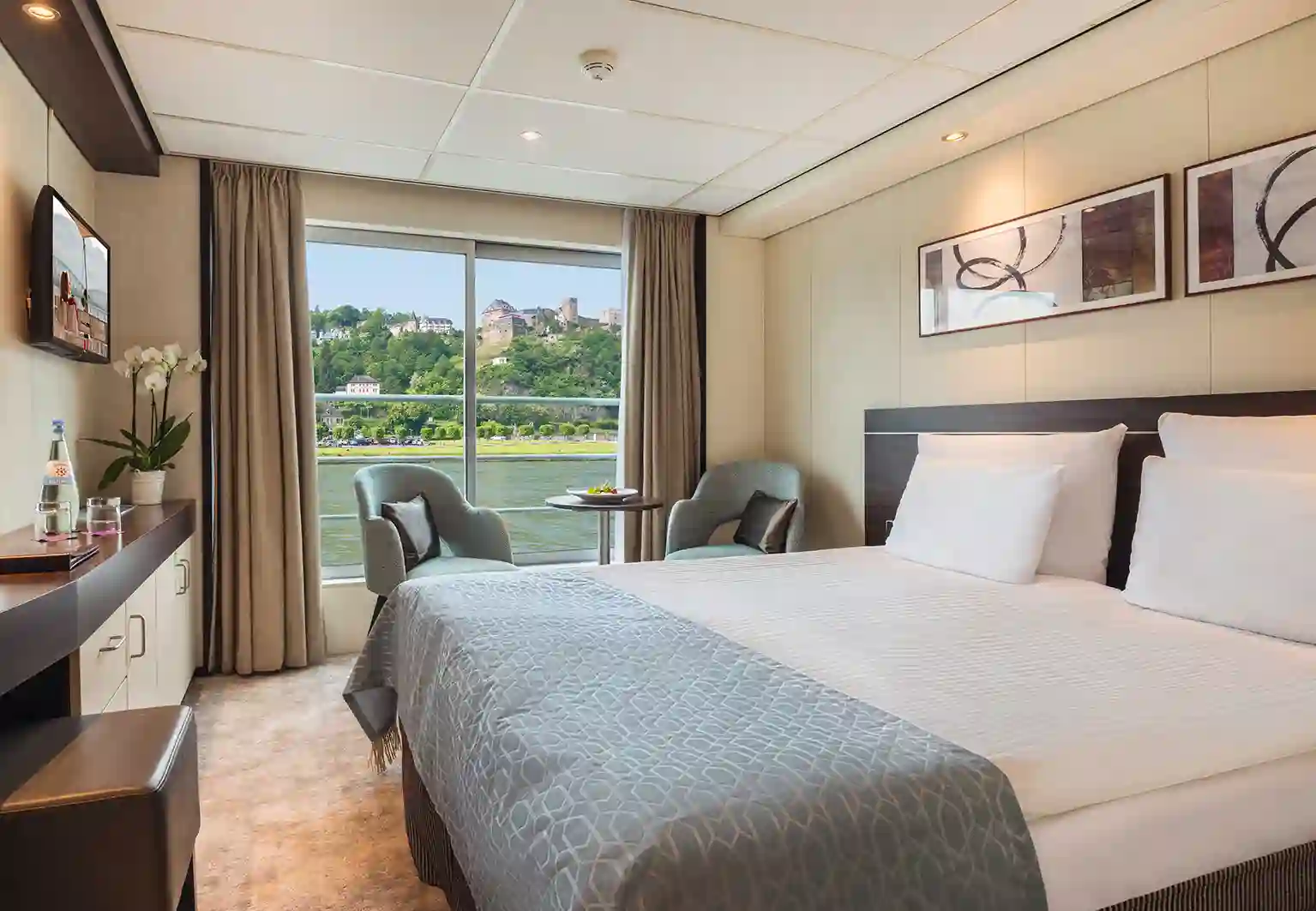 Kabine mit Doppelbett, bodentiefem Fenster, französischem Balkon, Sitzbereich und Blick auf den Fluss