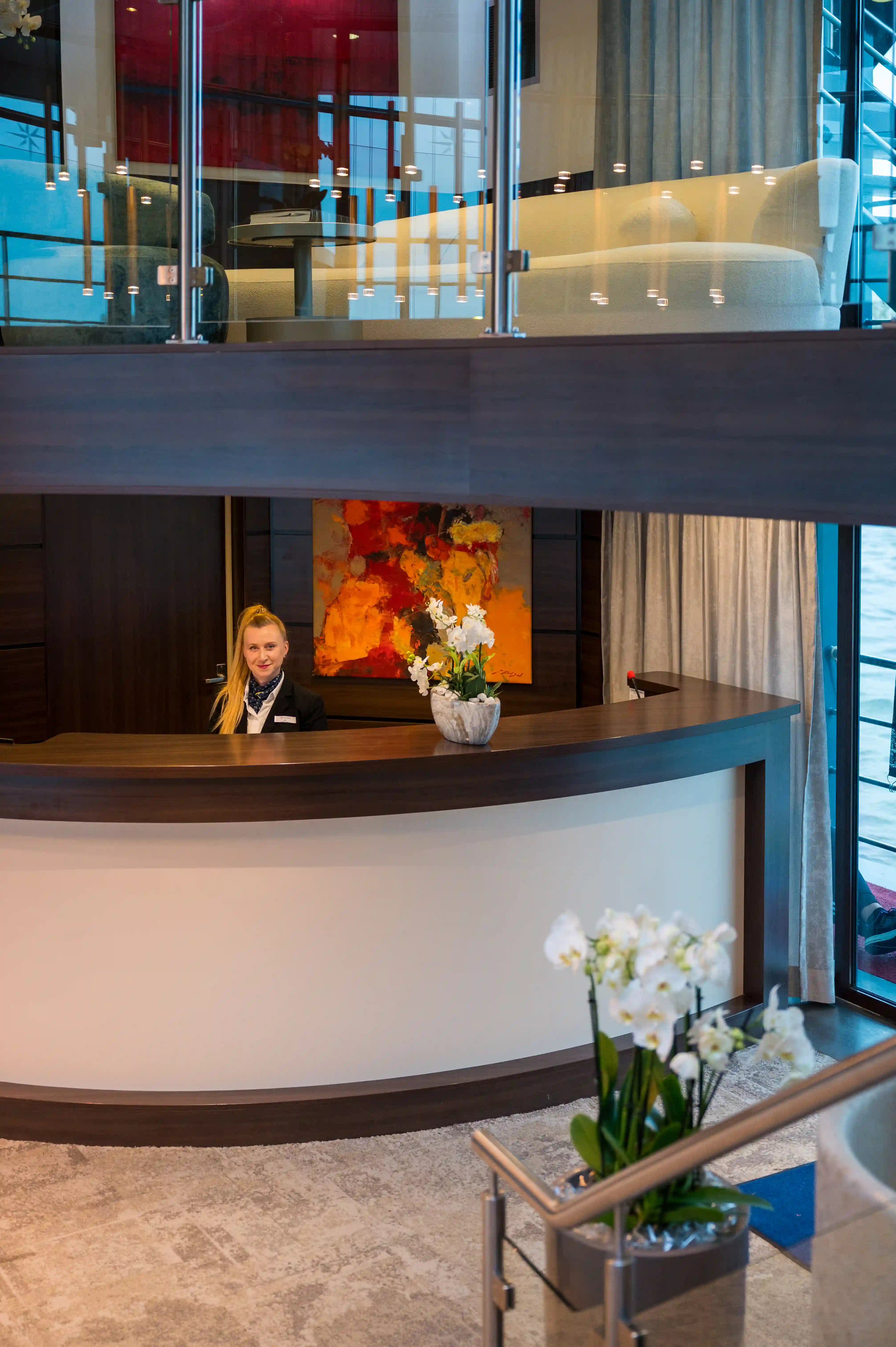 Rezeption mit gebogener Theke, freundlicher Mitarbeiterin, Blumendekoration und moderner Innenarchitektur