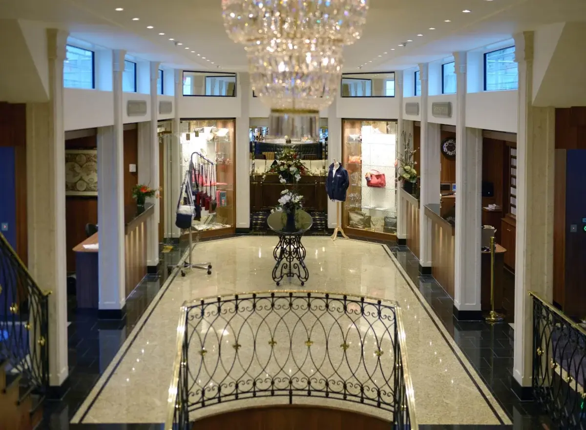 Elegante Lobby mit einer glänzenden Treppe, dunklem Holzboden und stilvoller Beleuchtung.