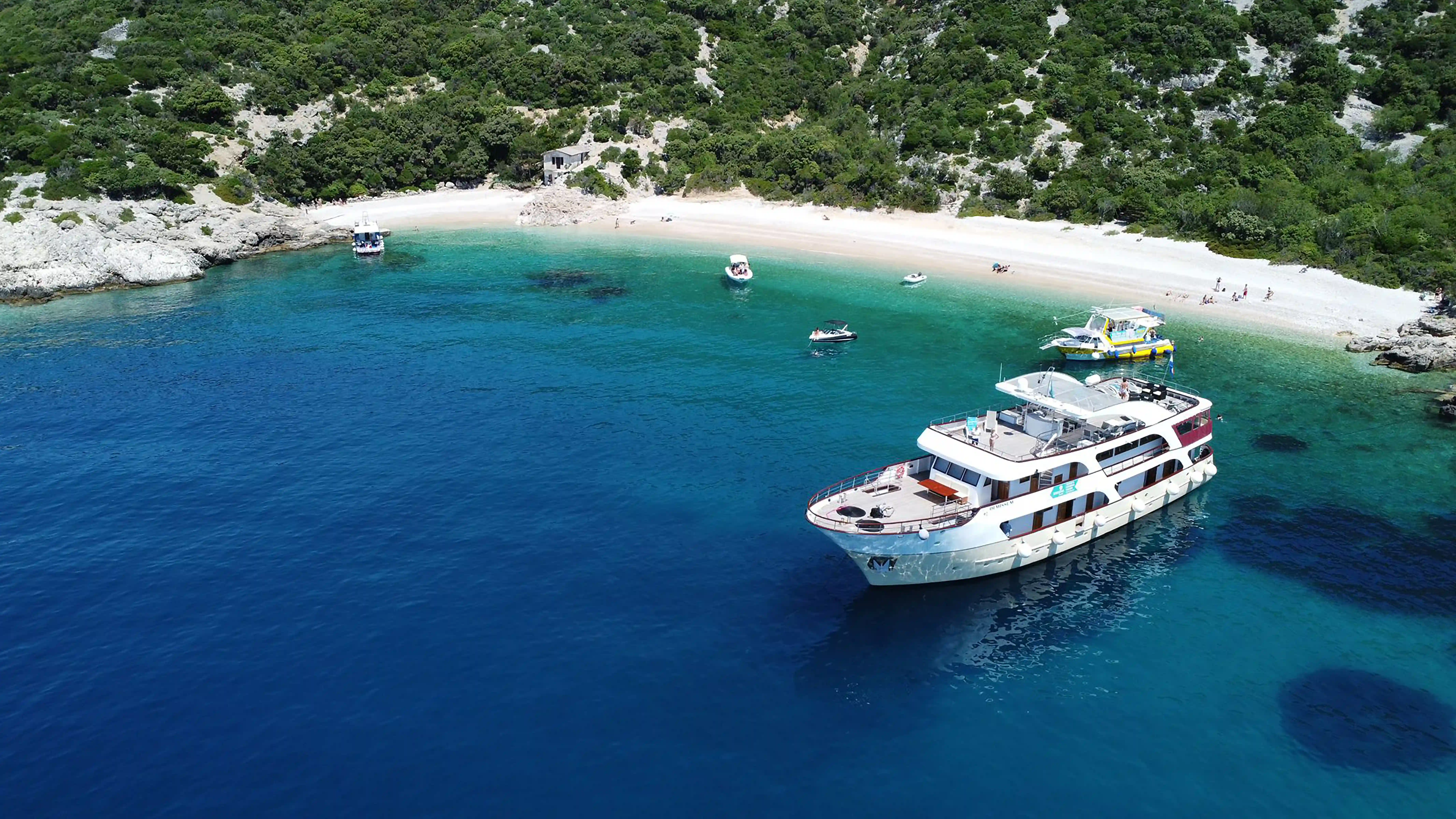 Kreuzfahrtschiff vor Anker in türkisfarbener Bucht mit Sandstrand