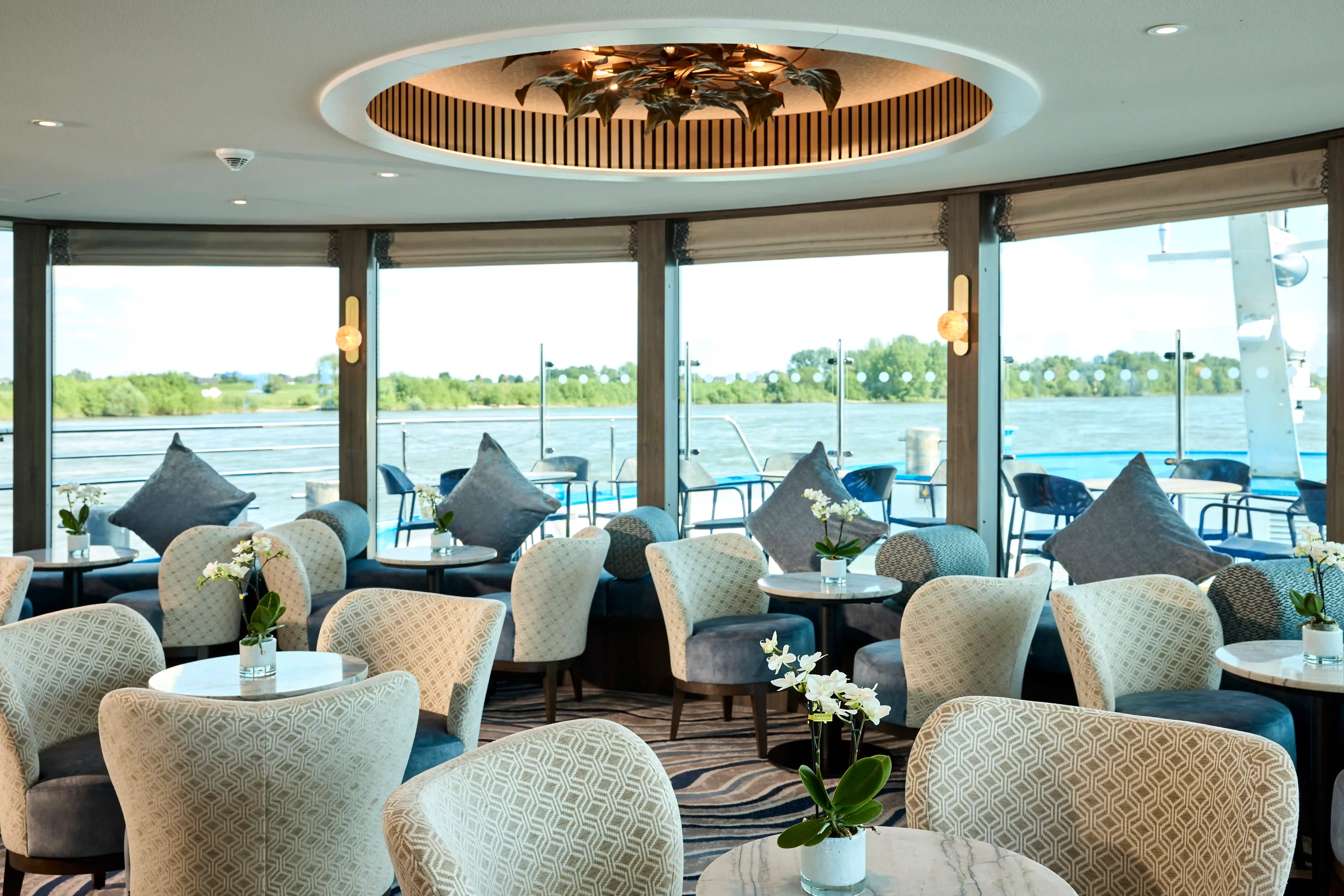 Elegante Lounge mit Sesseln, kleinen Tischen und großen Fenstern mit Blick auf den Fluss.