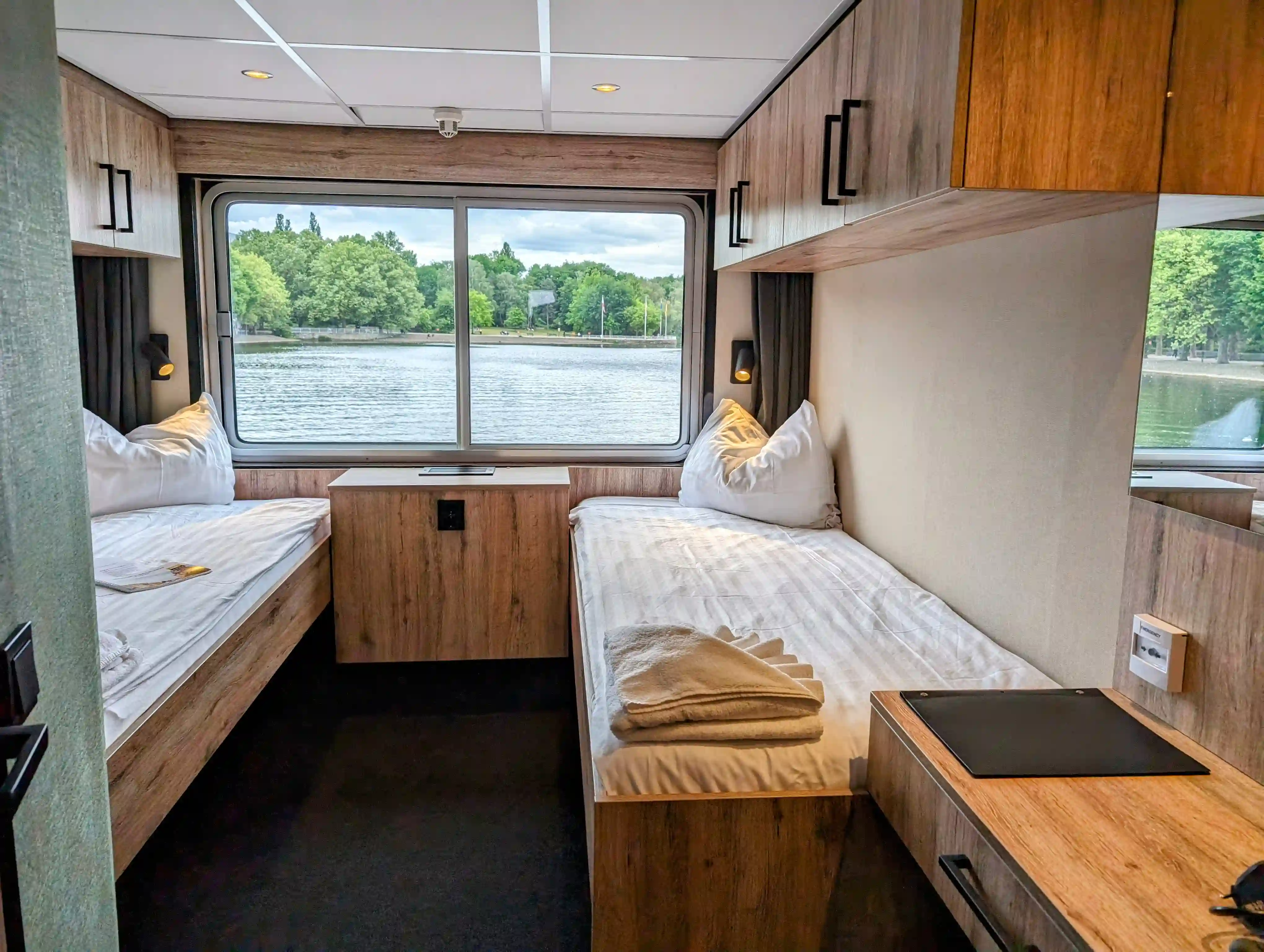 Kabine mit zwei Einzelbetten, grossem Fenster, Holzverkleidung und Blick auf Fluss und Bäume