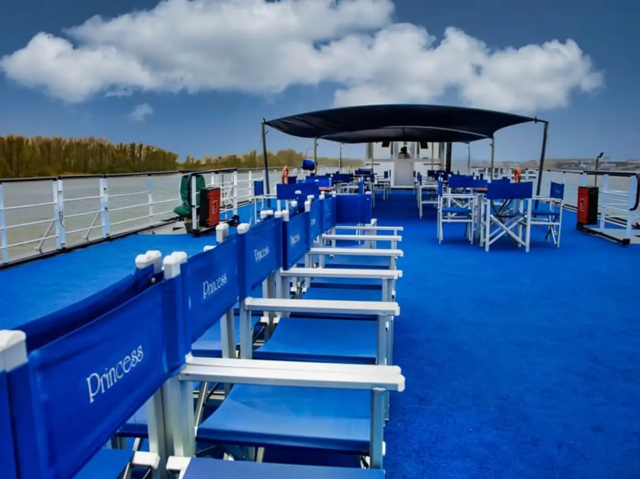Sonnendeck mit blauen Sitzstühlen, schattenspendender Überdachung und Blick auf Flusslandschaft