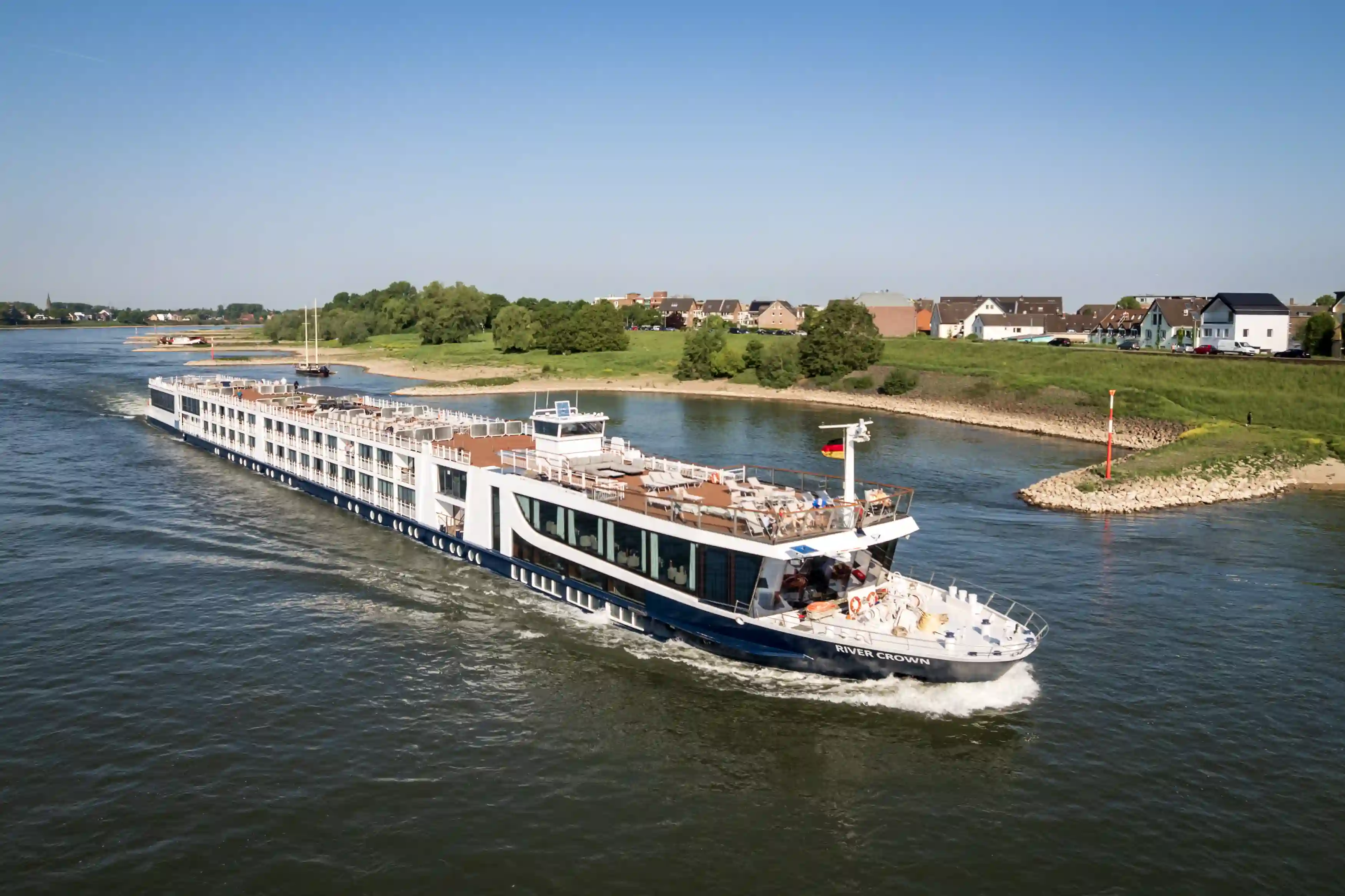 Elegantes Flusskreuzfahrtschiff fährt auf einem breiten Fluss durch eine grüne Uferlandschaft.