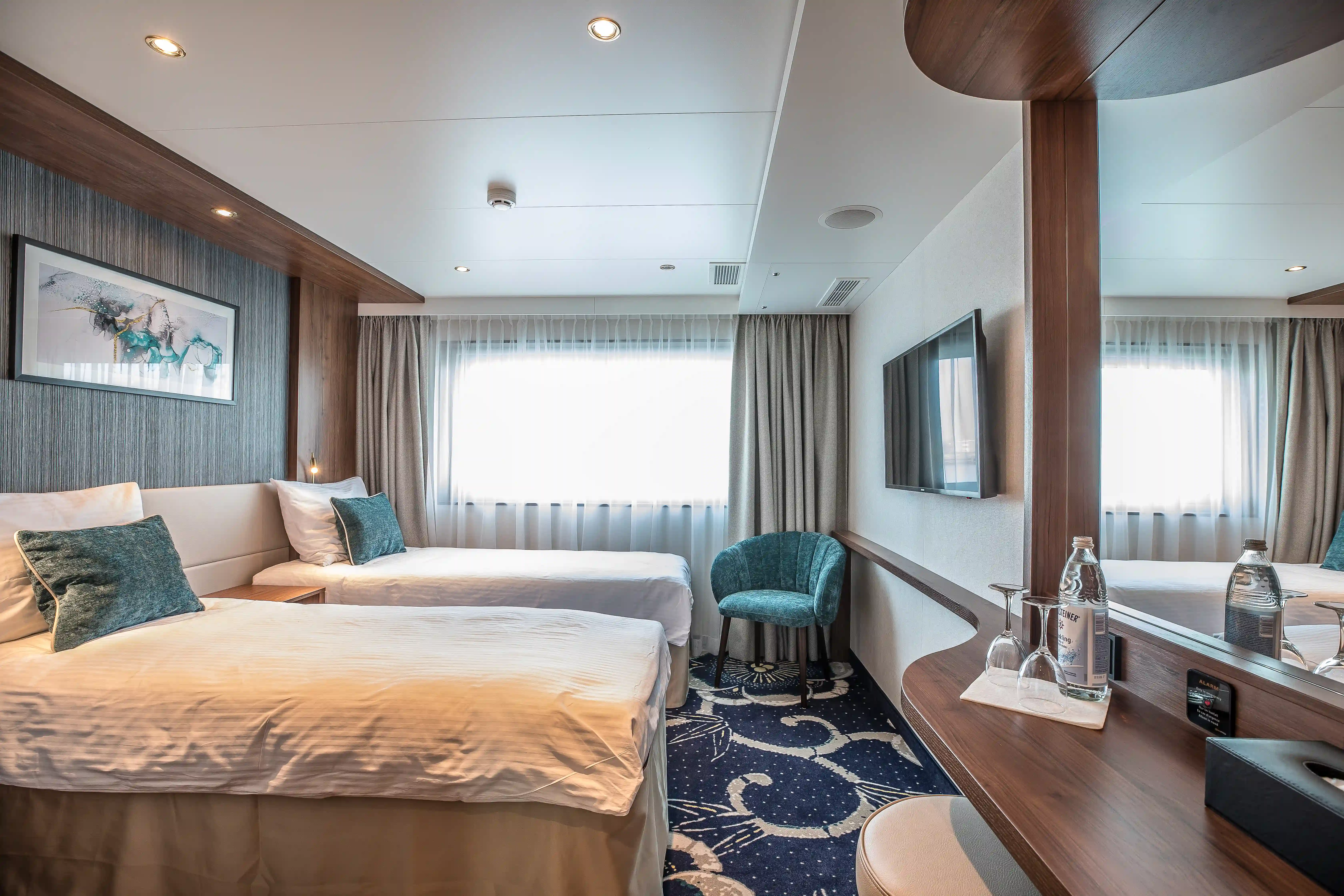 Helle Schiffskabine mit zwei Einzelbetten, Sessel, Spiegelwand und grossem Fenster