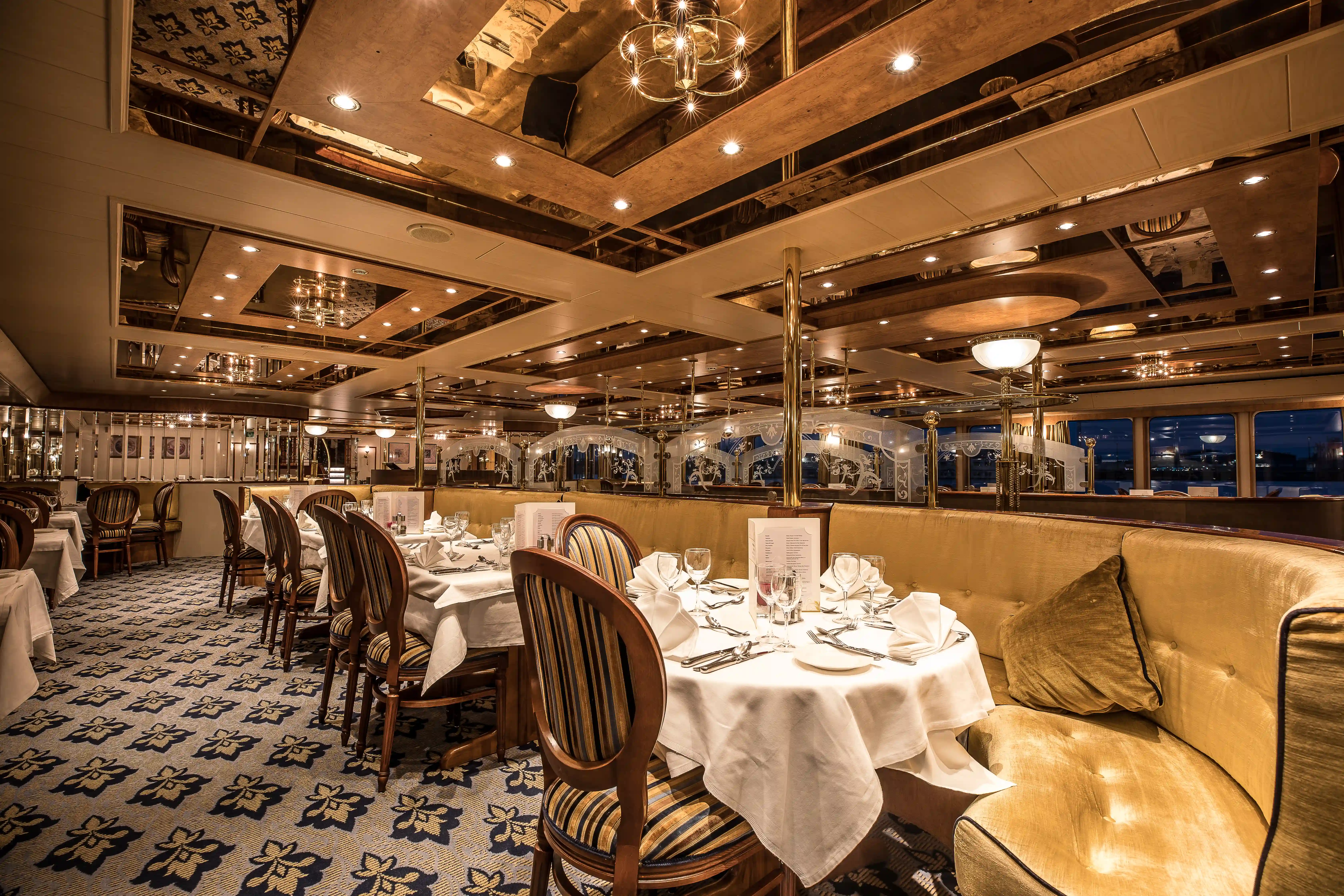 Grosszügiges Bordrestaurant mit runden Tischen, Stoffservietten, Polsterstühlen und dekorativer Beleuchtung