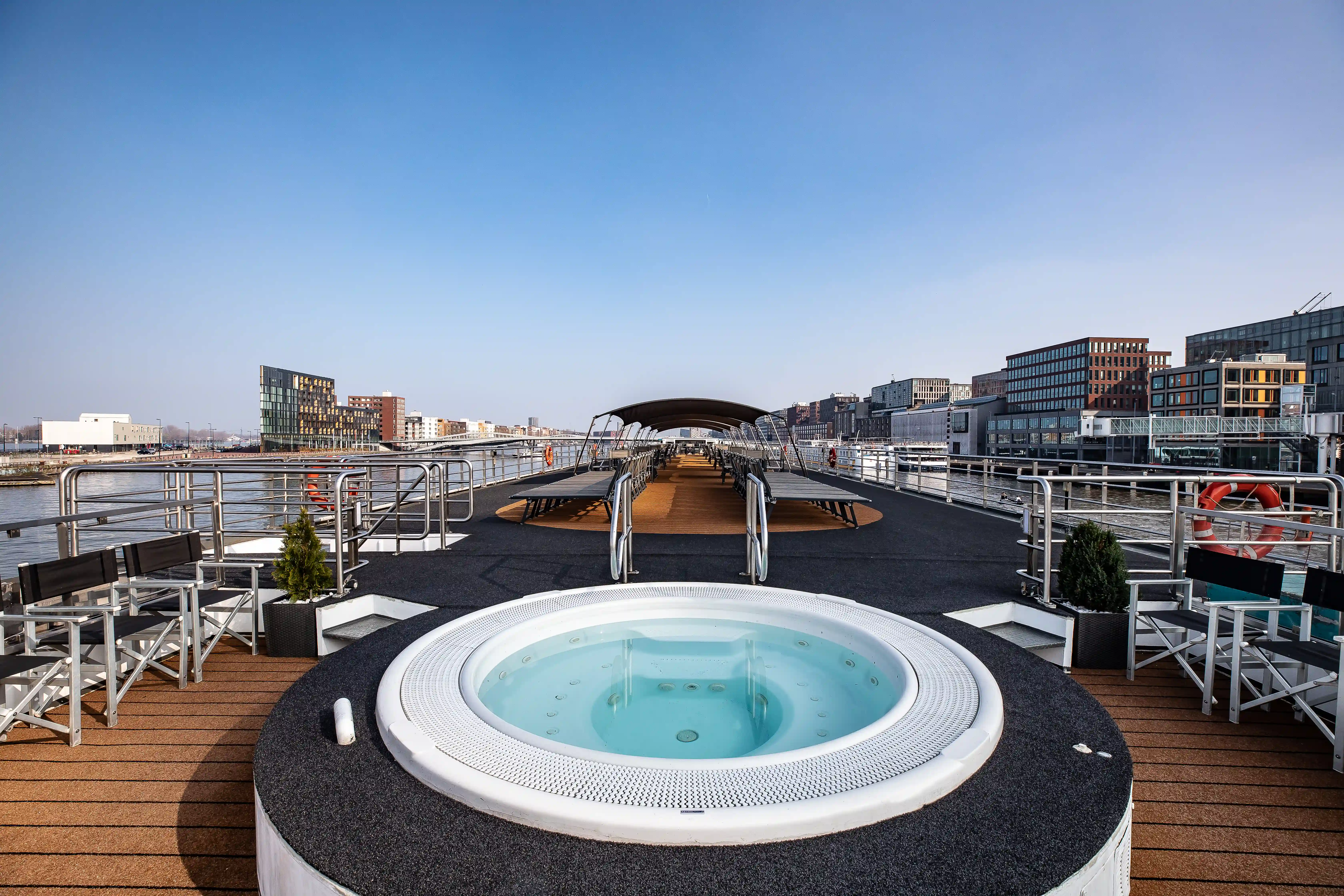 Sonnendeck mit rundem Whirlpool, umliegenden Liegestühlen, Geländern und weiter Aussicht auf die Stadt