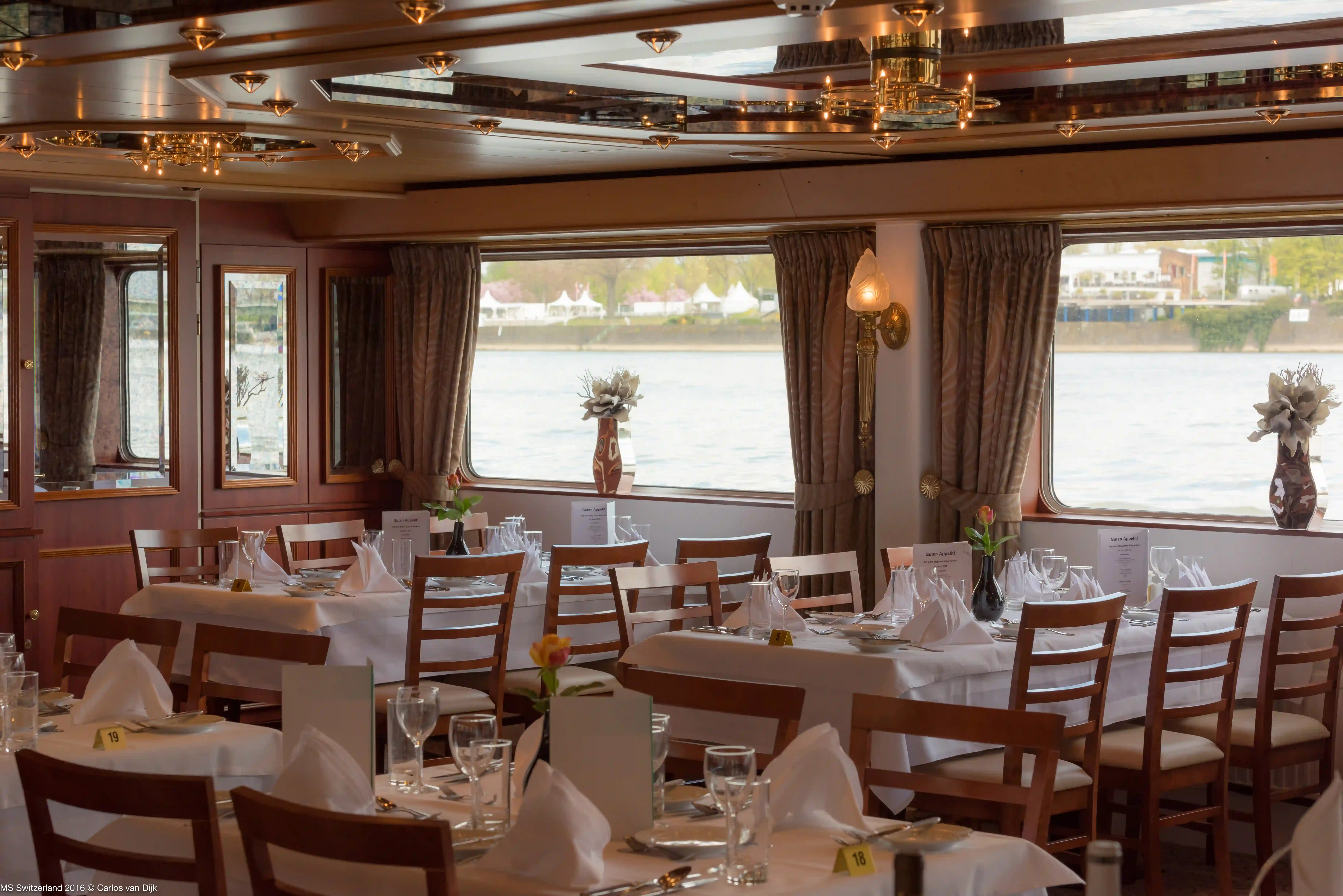 Blick in das stilvolle Schiffsrestaurant mit weiss gedeckten Tischen, Holzstühlen und grossen Fenstern mit Blick nach draussen.