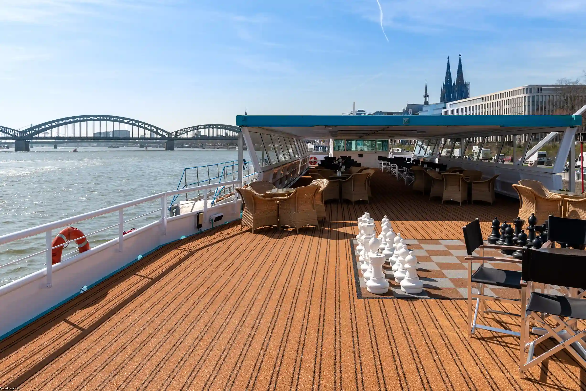 Blick über das Sonnendeck der MS Switzerland mit einem grossen Bodenschachspiel, Sitzgruppen und einem überdachten Bereich vor der Kulisse des Kölner Doms.