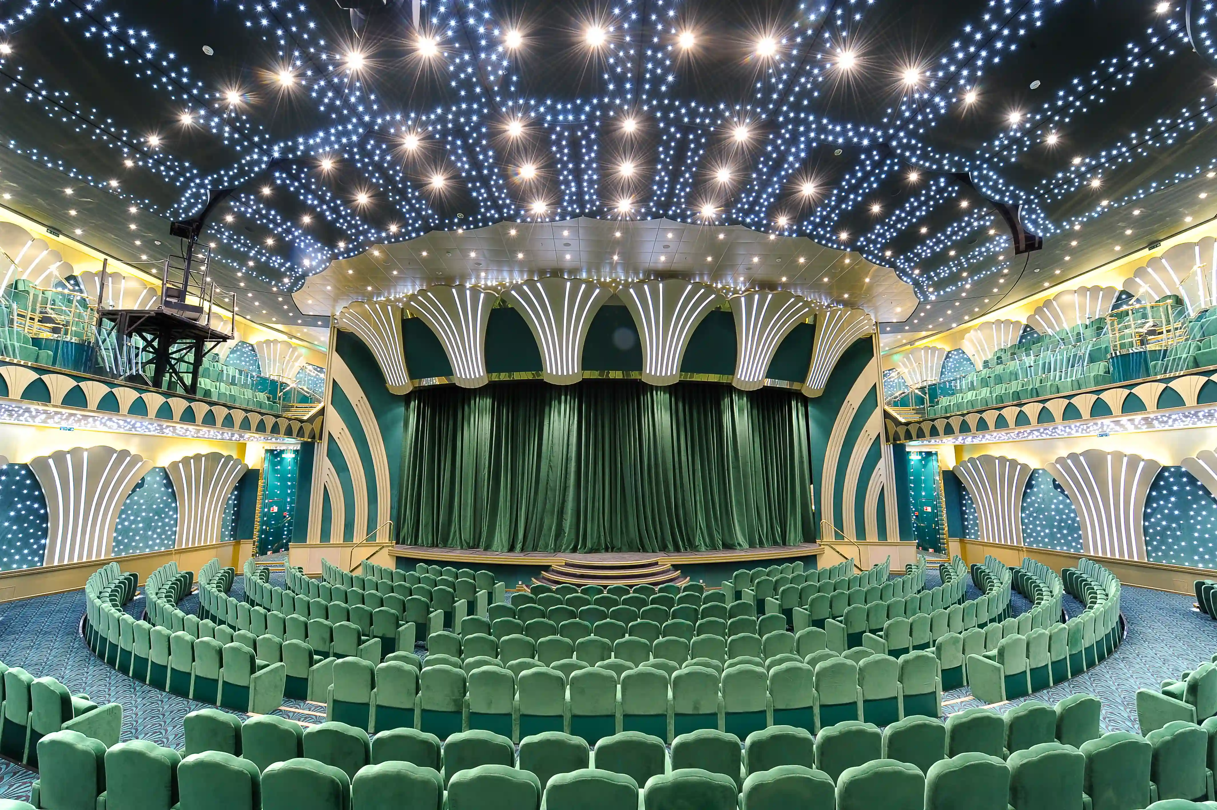 Grosses Theater der MSC Magnifica mit gruenen Sitzreihen, beleuchteter Decke und geschlossener Bühne.