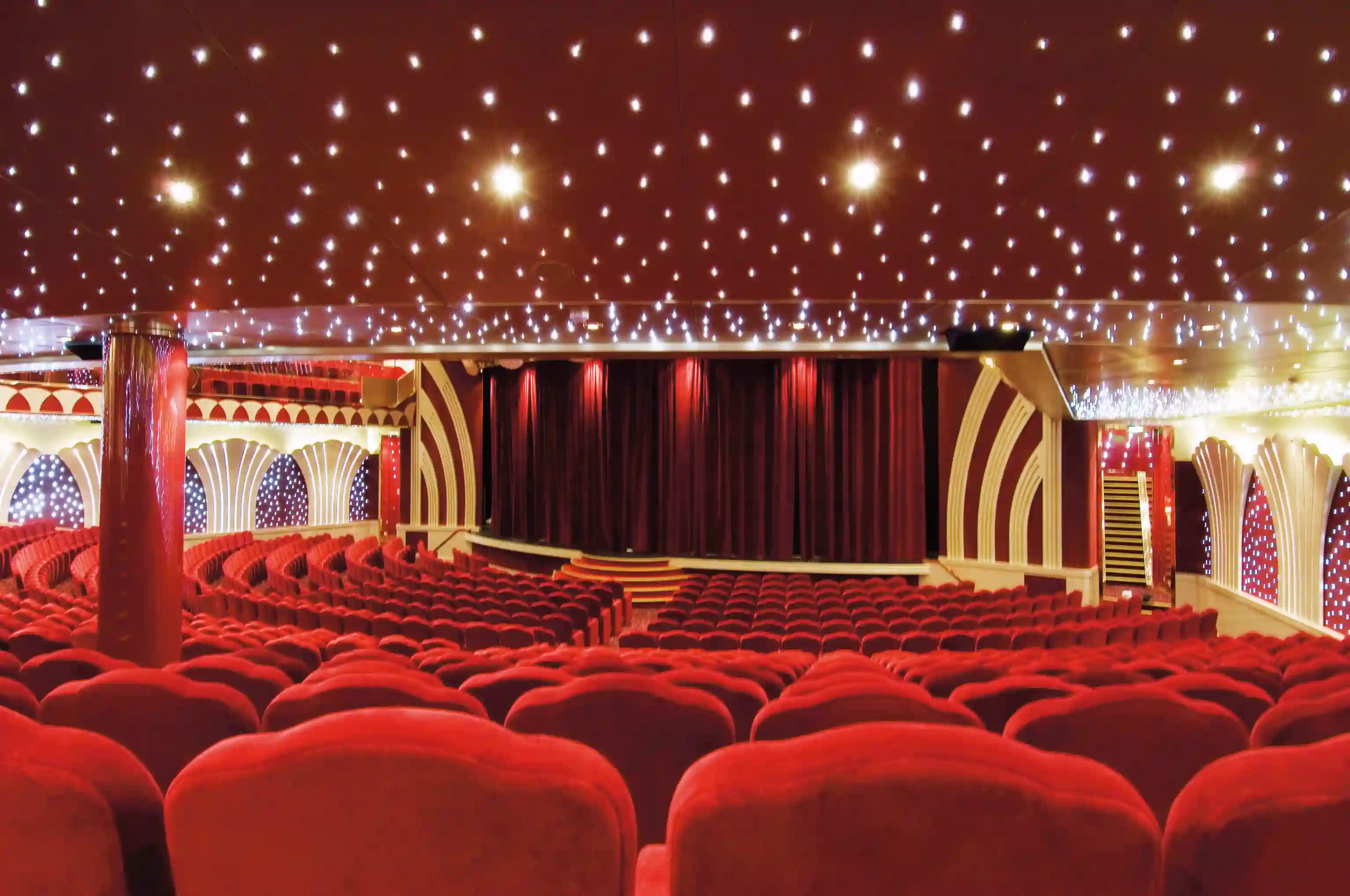 Theater der MSC Musica mit dekorativer Decke, warmem Licht, rotem Vorhang und geschwungener Buehne
