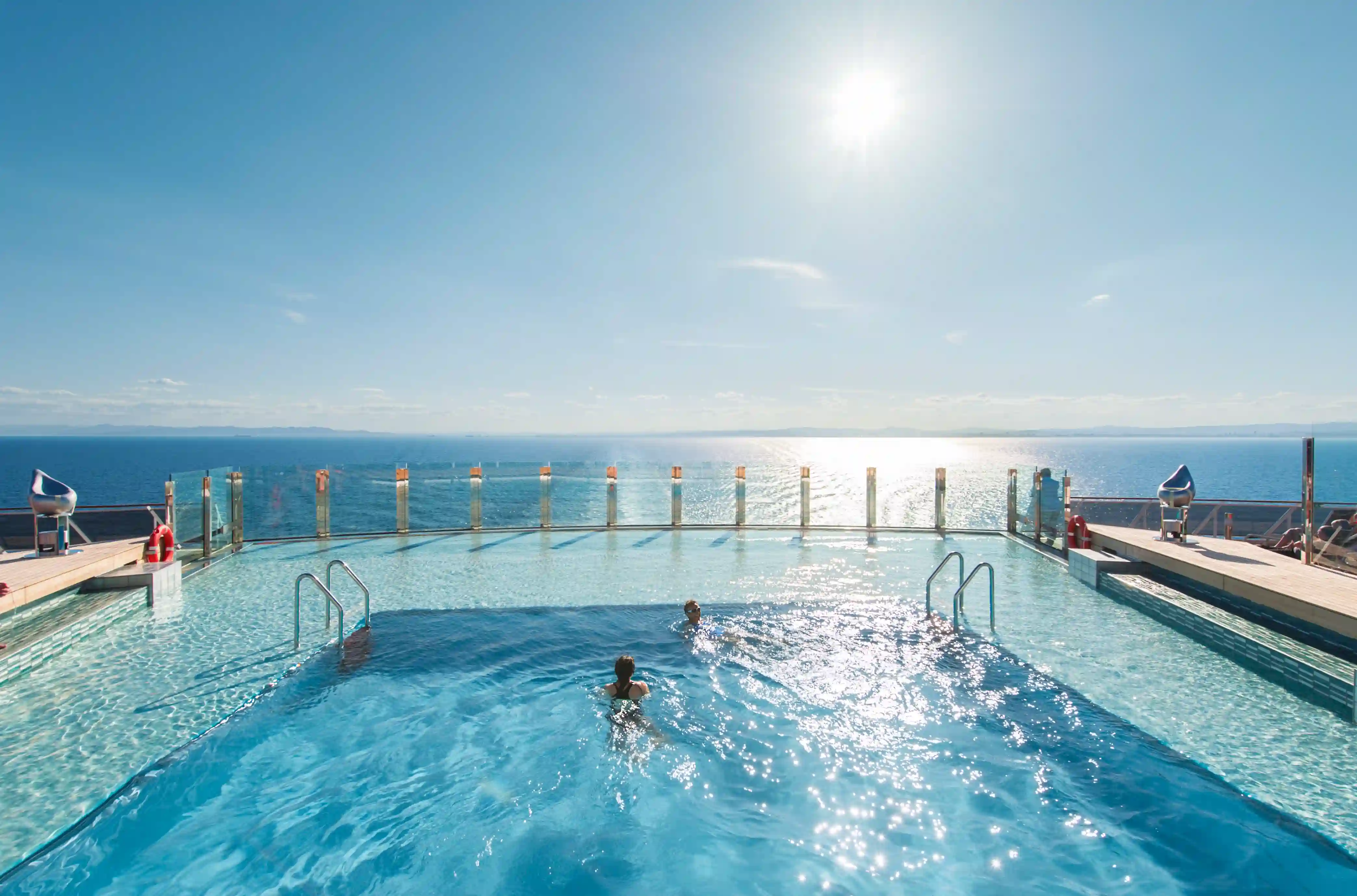 Aussenpool auf dem Sonnendeck der MSC Preziosa mit Blick auf das Meer, klarem Himmel und schwimmenden Gaesten