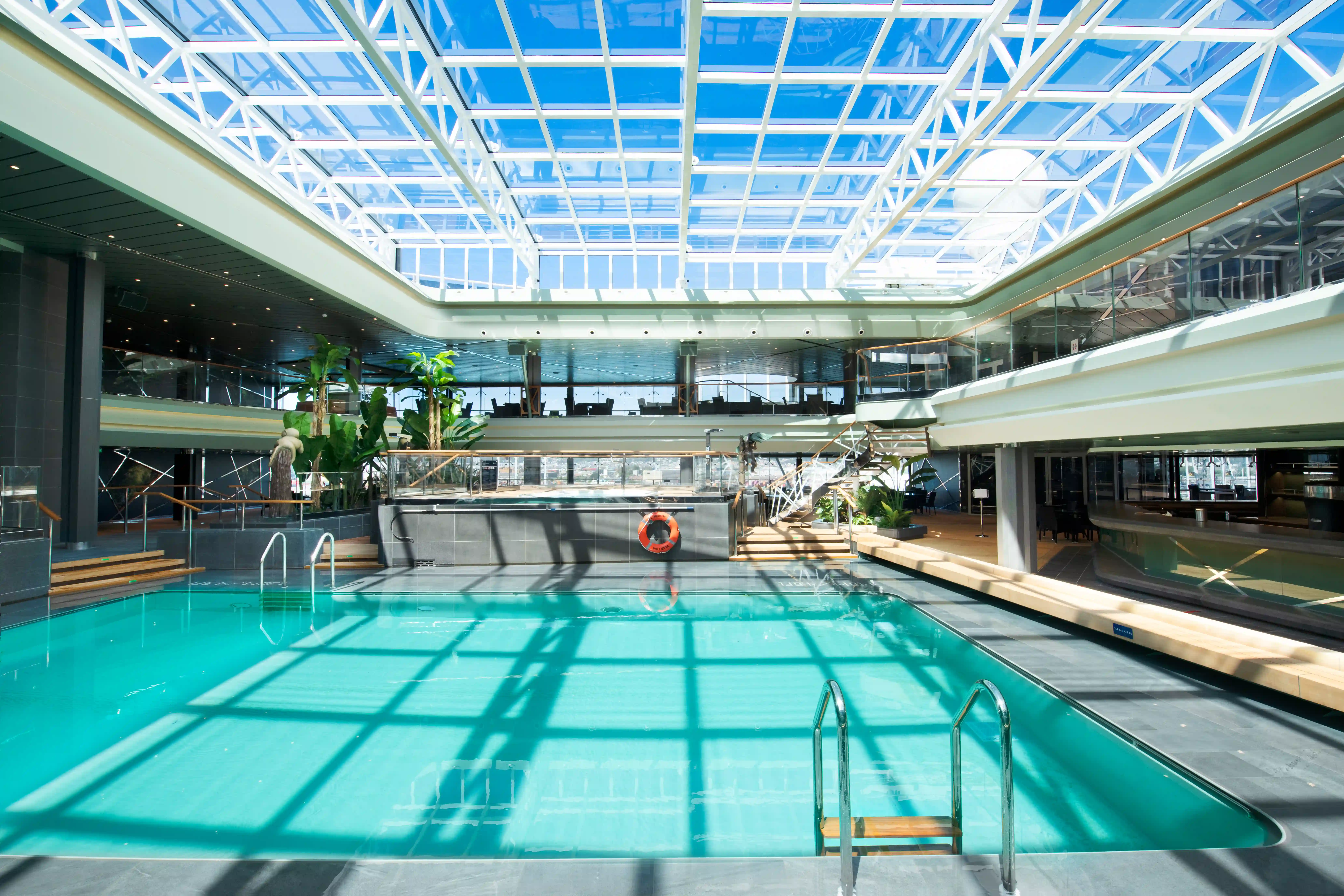 Innenpool auf der MSC Virtuosa mit Glasdach, Pooltreppe und umliegenden Sitzbereichen