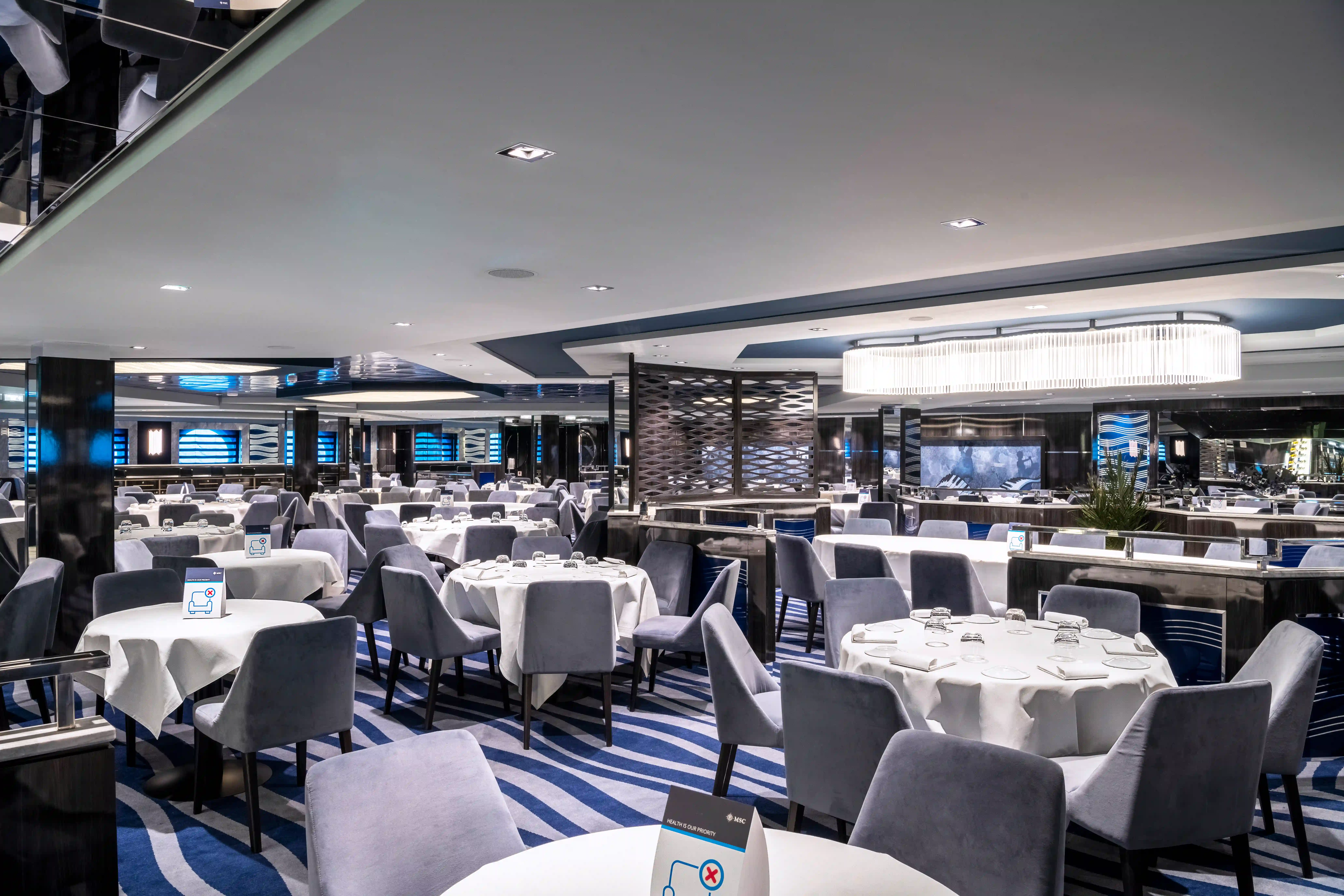 Elegantes Restaurant auf der MSC Virtuosa mit gedeckten Tischen, Polsterstühlen und moderner Beleuchtung