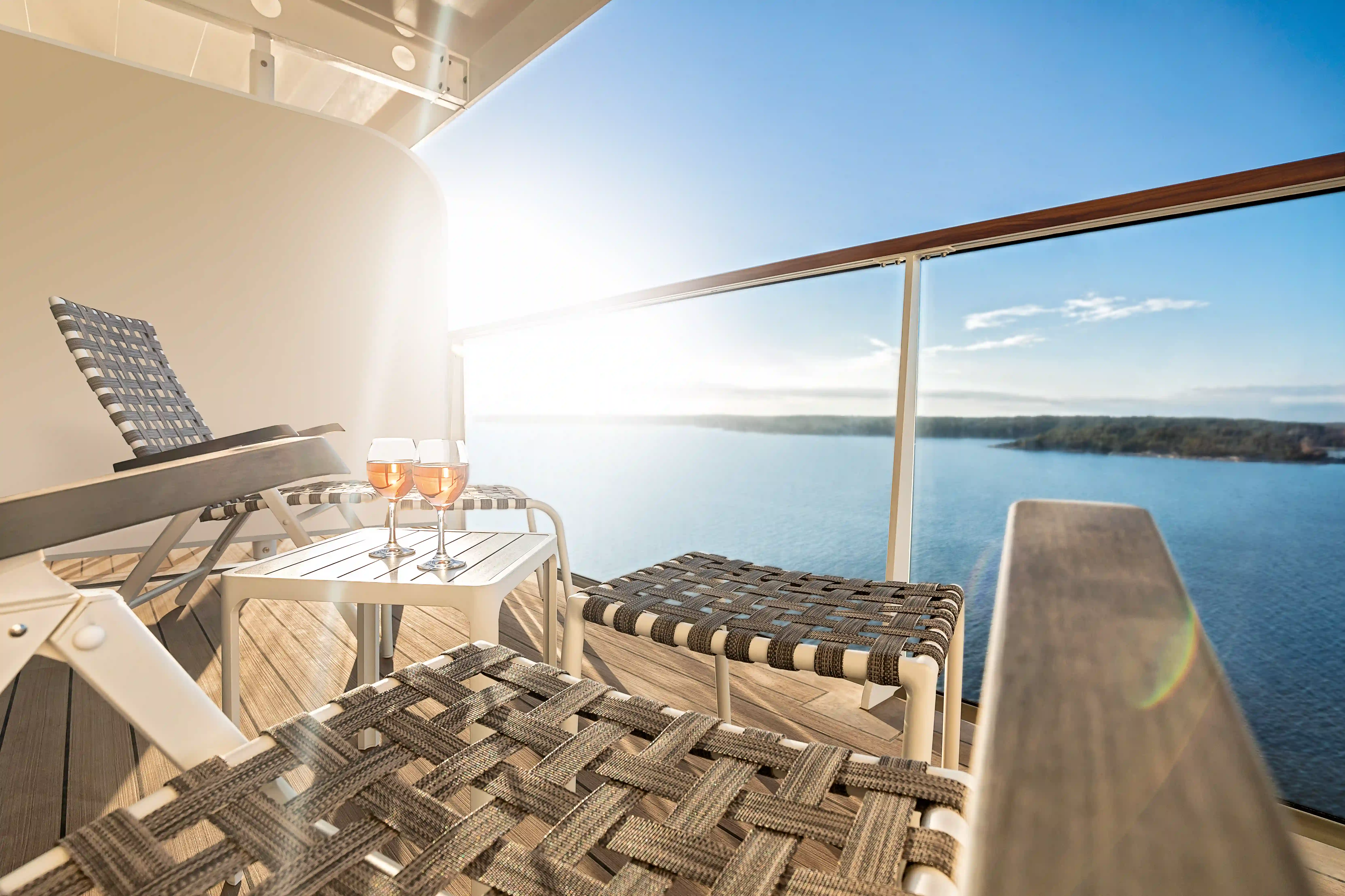 Balkon mit Liegen, kleinem Tisch und Gläser, Blick auf das Meer bei Sonnenschein