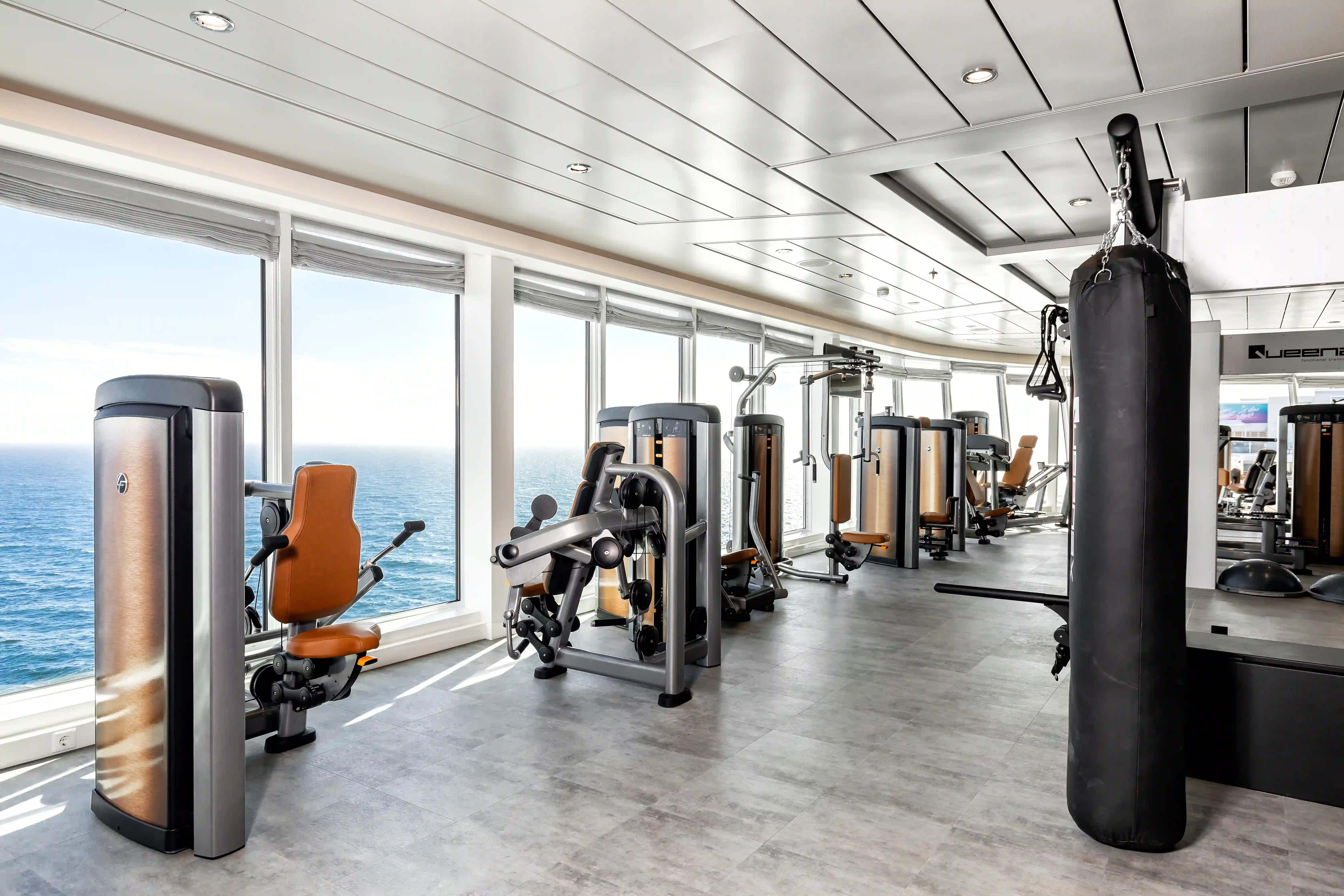 Fitnessraum mit Trainingsgeräten, Boxsack und Panoramafenstern mit Meerblick