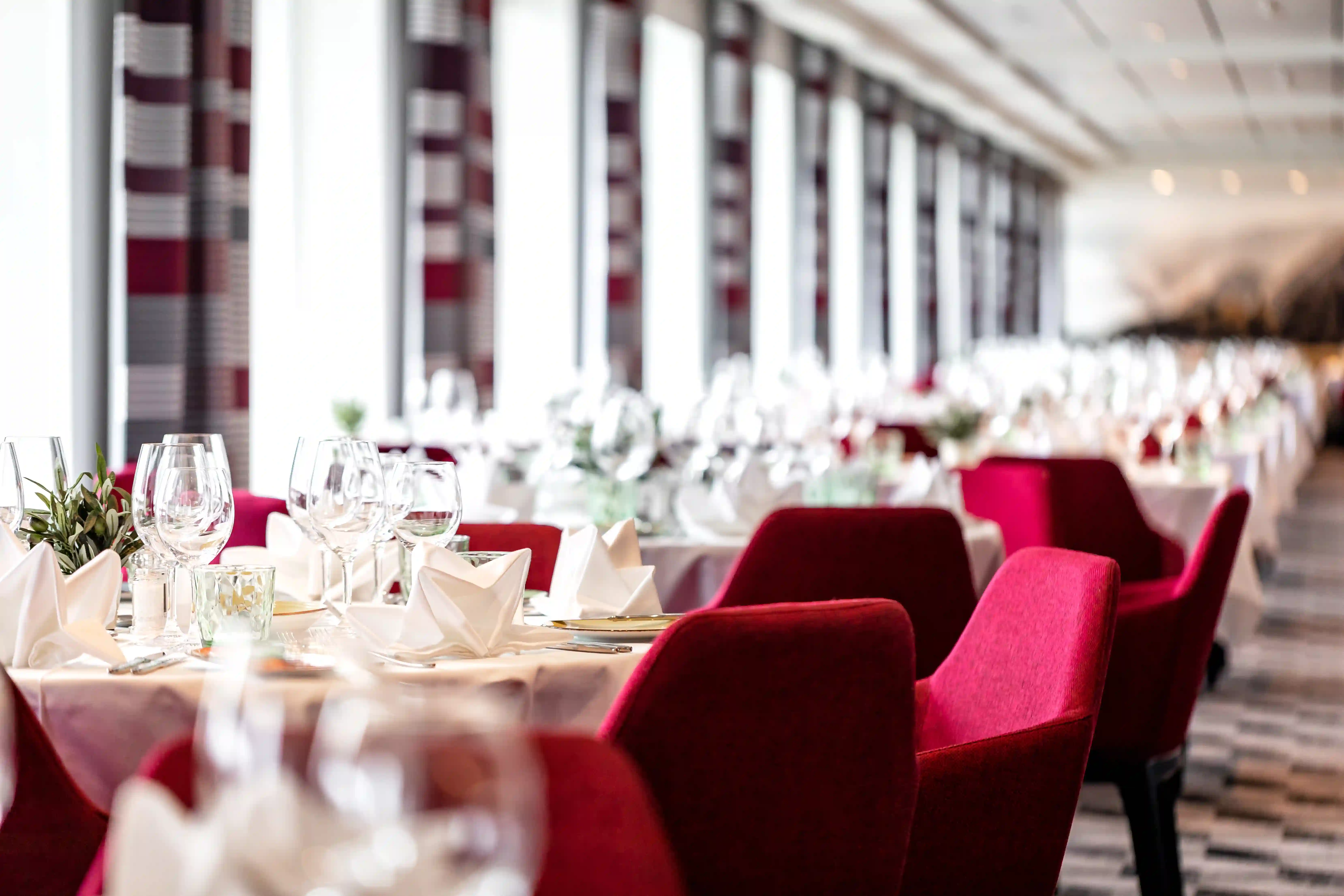 Elegantes Restaurant mit gedeckten Tischen, roten Sesseln und grossen Fenstern