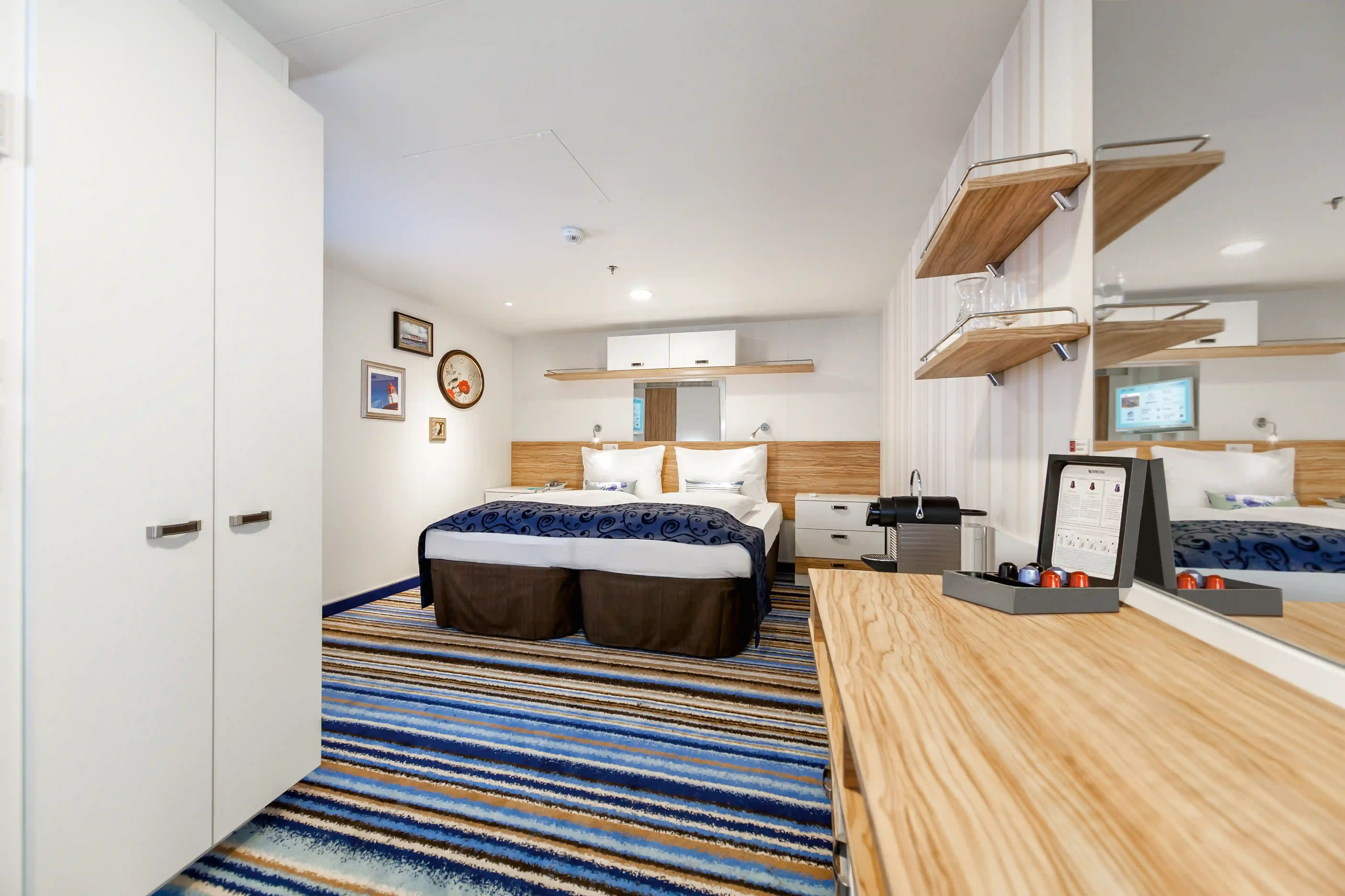 Innenansicht einer Innenkabine auf der Mein Schiff 3 mit einem Doppelbett, einem Kleiderschrank, einem Schreibtisch und einer Nespresso-Maschine.