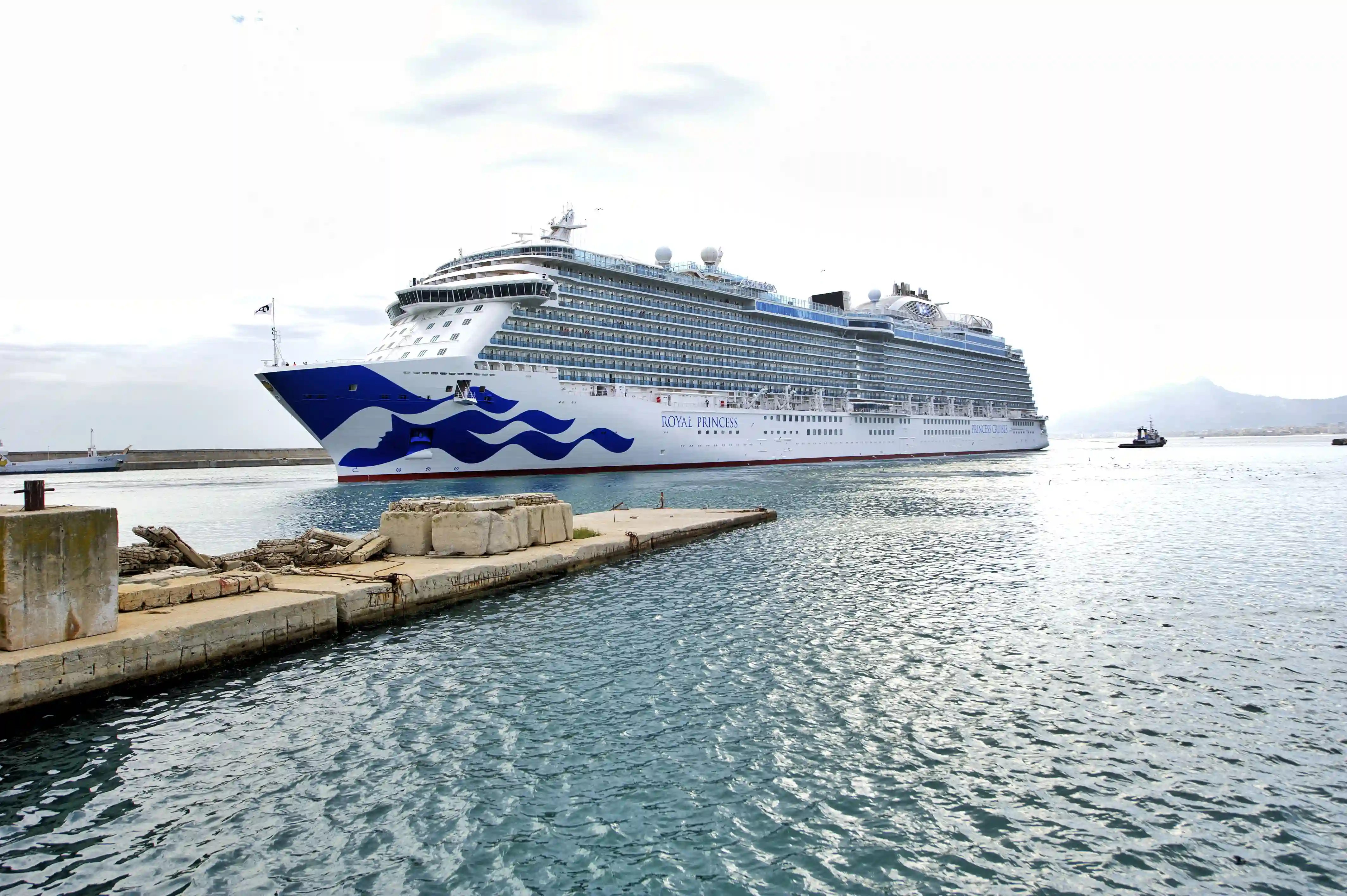 Das Kreuzfahrtschiff Royal Princess liegt an einer Hafenmole im ruhig fließenden Wasser unter leicht bewölktem Himmel.