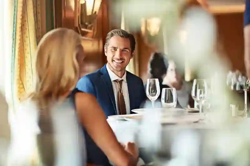 Ein lächelndes Paar in feiner Abendkleidung sitzt an einem weiß gedeckten Tisch im Restaurant des Kreuzfahrtschiffes.