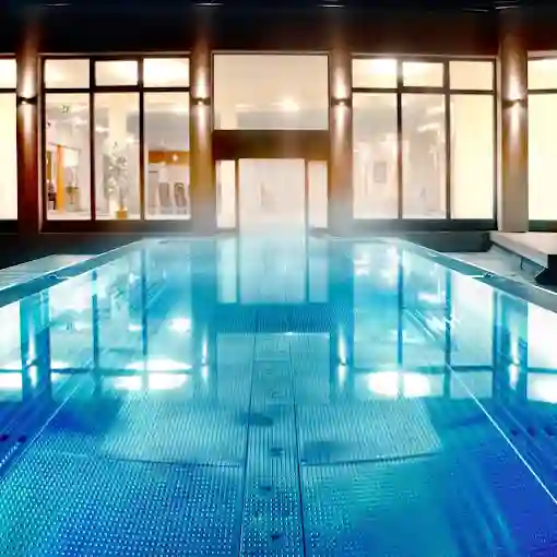 Heller Innenpool eines Hotels mit klarem Wasser, moderner Architektur, grossen Fensterflaechen und ruhiger Wellnessatmosphaere.