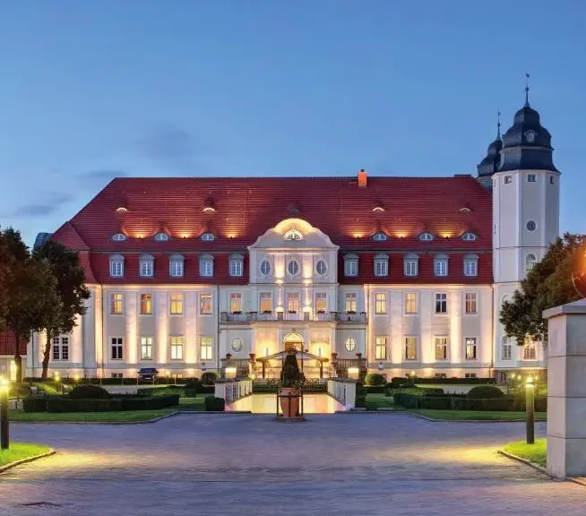Schlosshotel Fleesensee mit beleuchteter Fassade und gepflegter Gartenanlage in der Abenddämmerung.