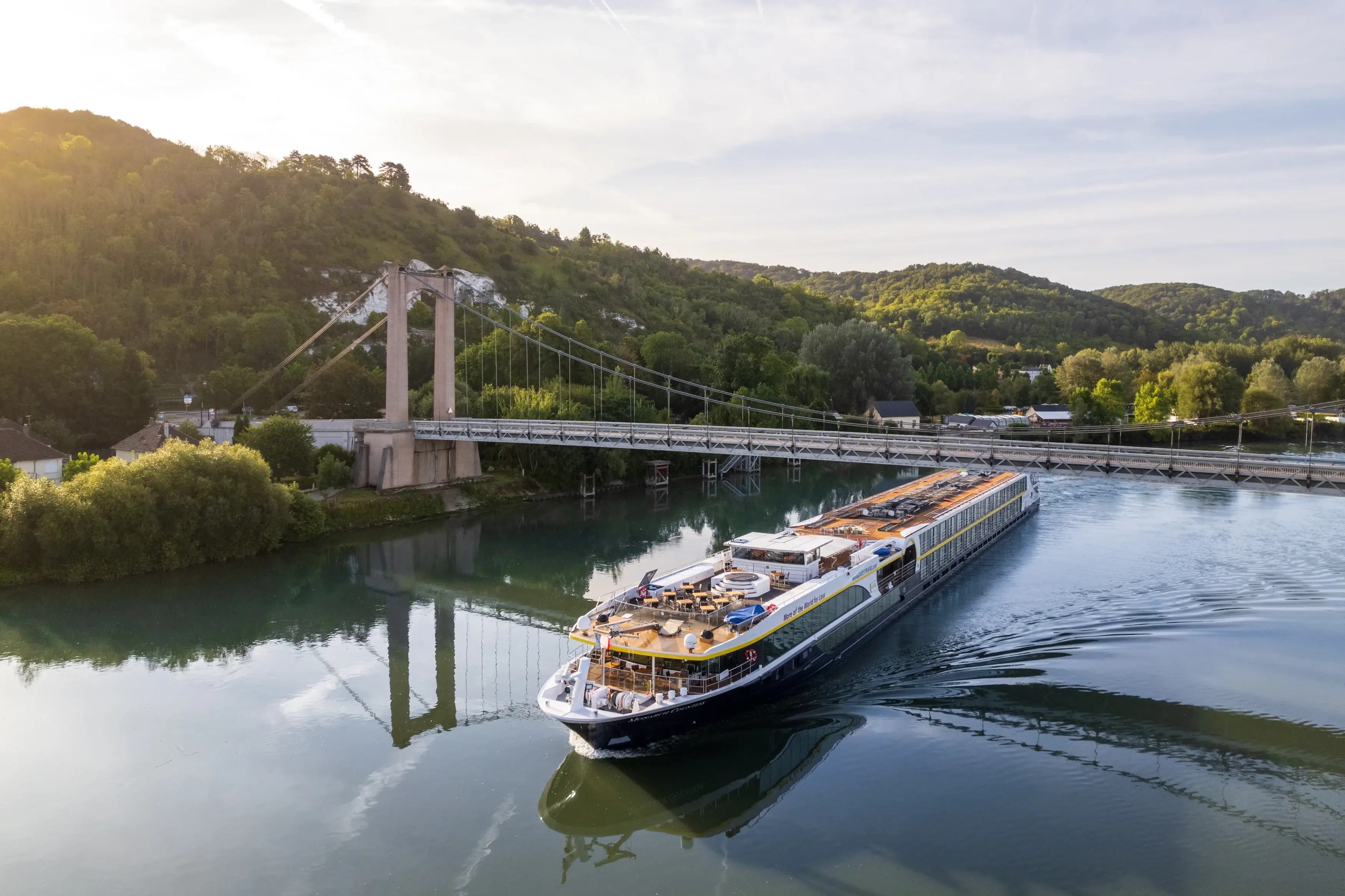 Le MS Monarch Countess passe sous un pont suspendu sur une riviere paisible au coeur d un paysage vallonne verdoyant.