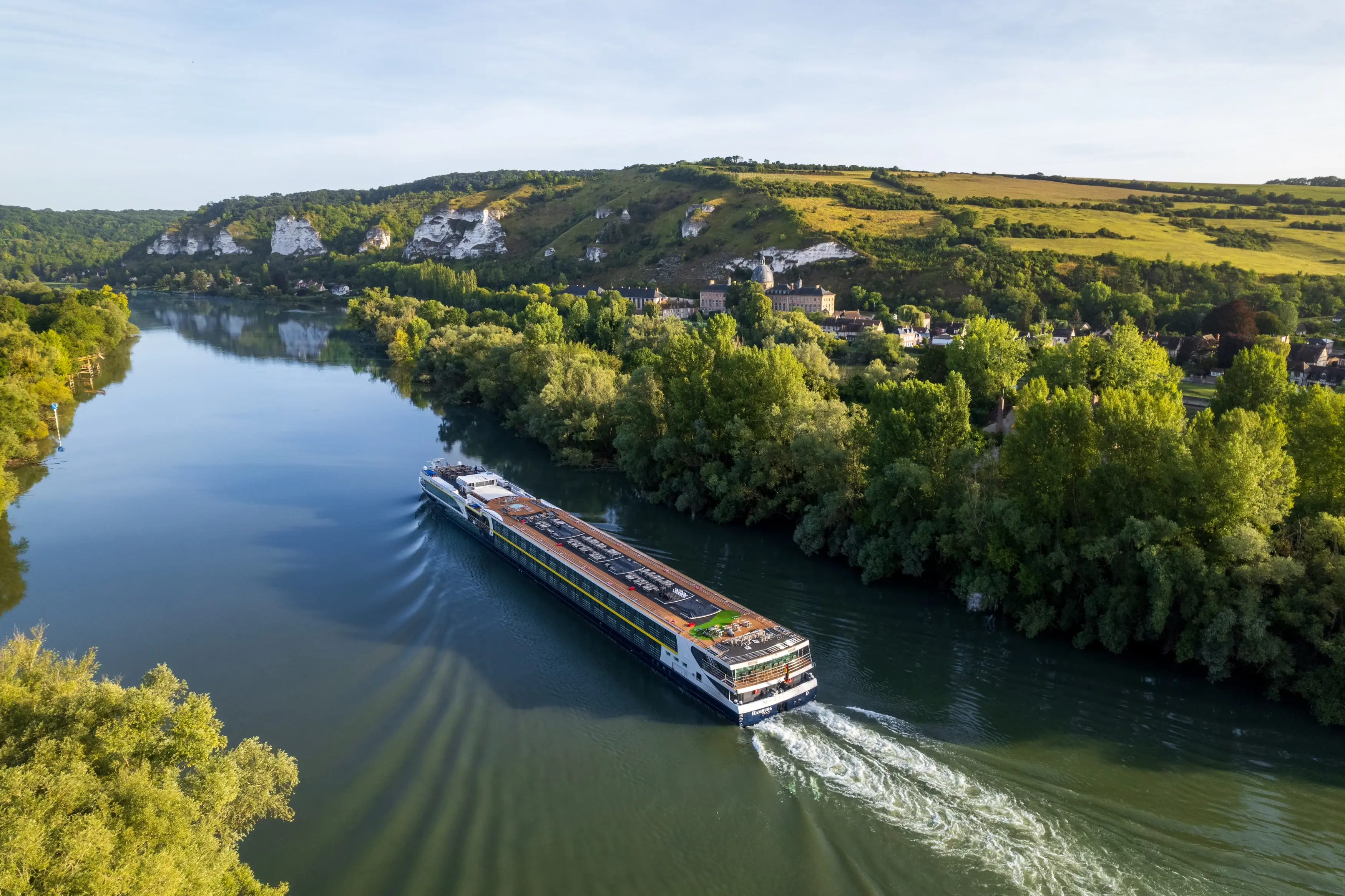 Le MS Monarch Countess navigue dans un vaste paysage fluvial borde de forets avec des falaises calcaires en arriere plan.