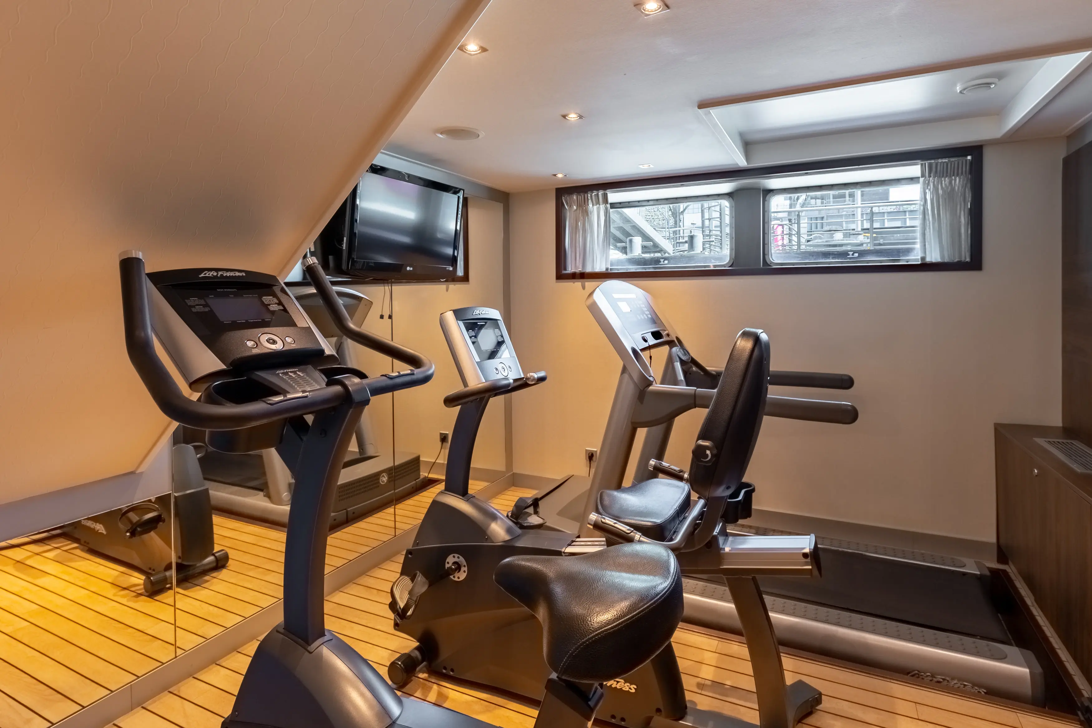 Salle de remise en forme a bord du MS Monarch Countess avec appareils de cardio, miroir mural et televiseur.