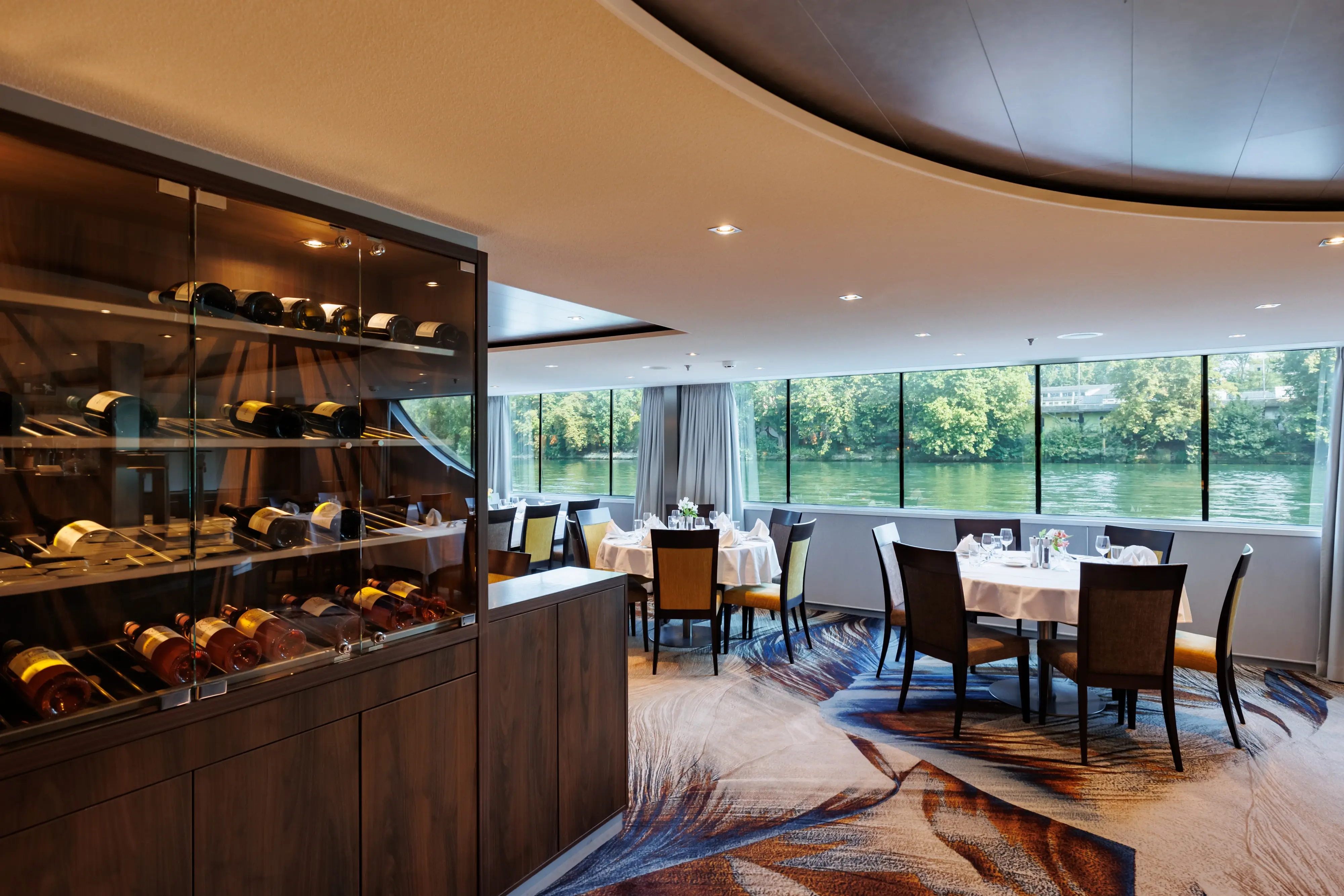 Espace restaurant du MS Monarch Countess avec cave a vin et vue panoramique sur le paysage fluvial.